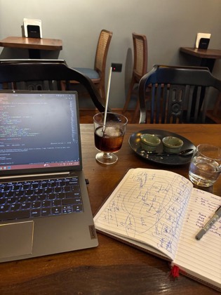 A laptop showing code beside a cold brew and a notebook covered in hand-drawn diagrams