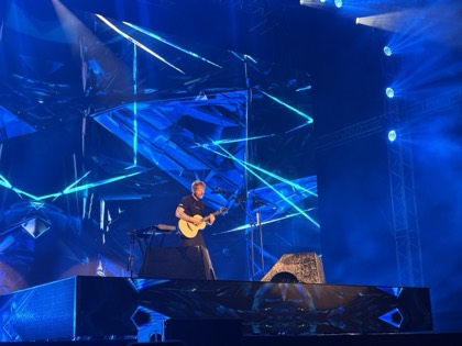 Ed Sheeran alone on a blue-lit stage with an acoustic guitar