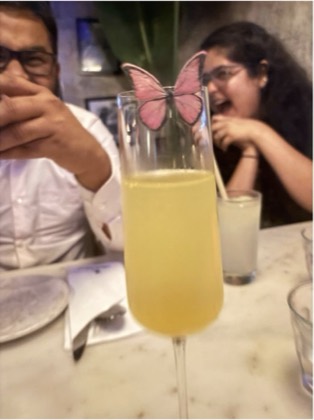 Partho and Tanisha laughing behind a cocktail glass decorated with a pink butterfly