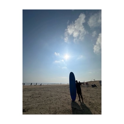 A surfer silhouetted beside an upright board on a bright empty beach