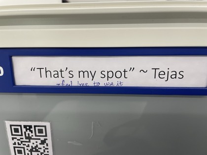 A laminated office sign reading That's my spot, Tejas, with feel free to use it added underneath in pen